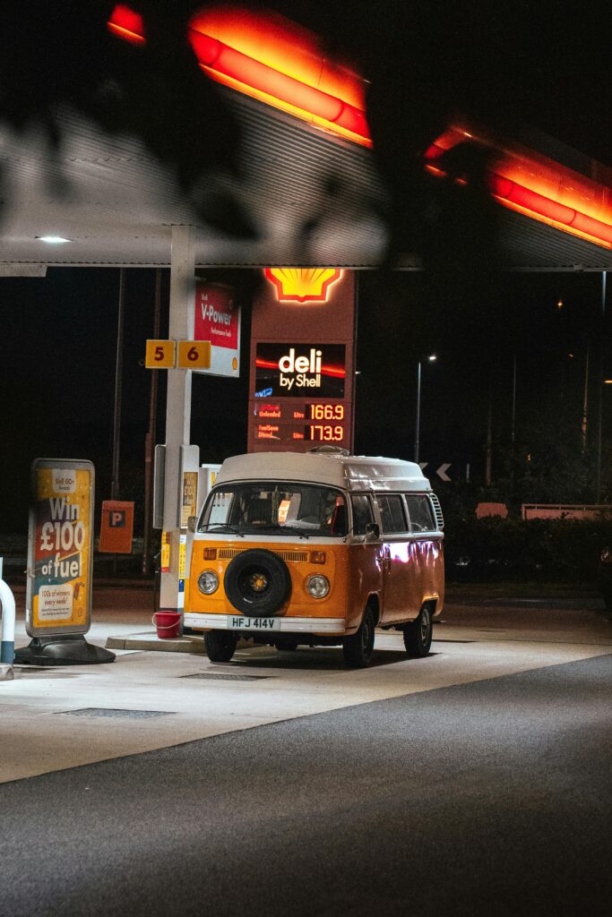 Vintage orange VW camper parked at a brightly lit Shell gas station at night.