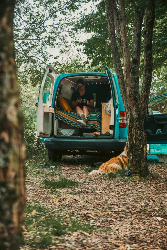 Woman relaxes in a camper van with a dog, embracing van life in a serene forest setting.