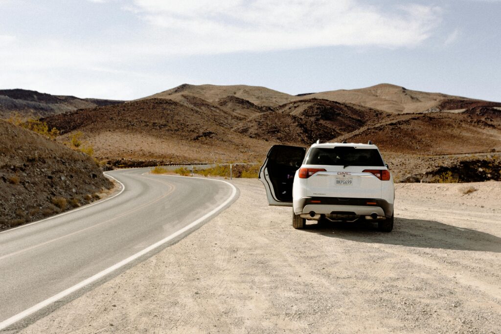 White SUV parked along a winding desert road under clear skies, showcasing adventure and travel.